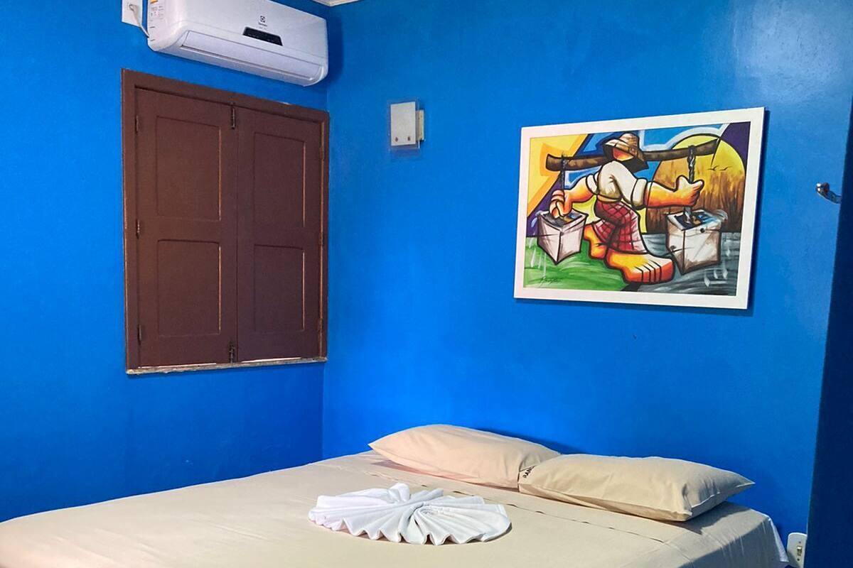A room with a bed, a painting, an air conditioning unit, and a door.