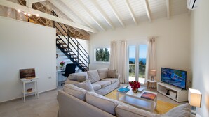 Un salon moderne avec un canapé, une table basse et un téléviseur. Un escalier mène à un niveau supérieur.