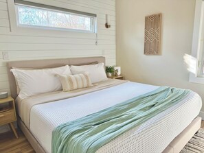 Een netjes opgemaakt bed met een lichtkleurig hoofdeinde, een nachtkastje met een lamp en een raam met blinds.