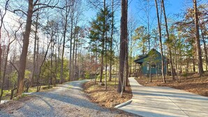 A forested area with a gravel path leading to a small building with a porch. - The Stone - Modern Cabin on 40+ acres, 10 mins from Tryon Equestrian Center TIEC (Rutherfordton)