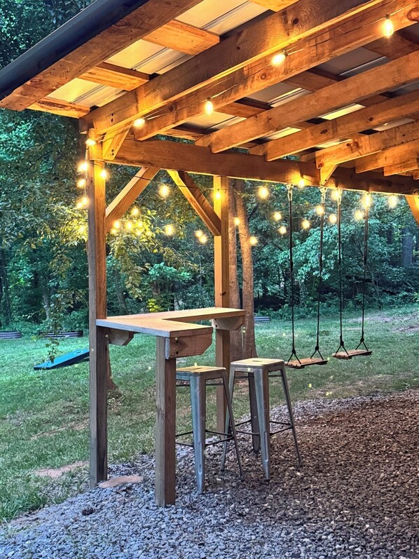 Une pergola en bois, décorée de guirlandes lumineuses, avec une table et deux chaises.