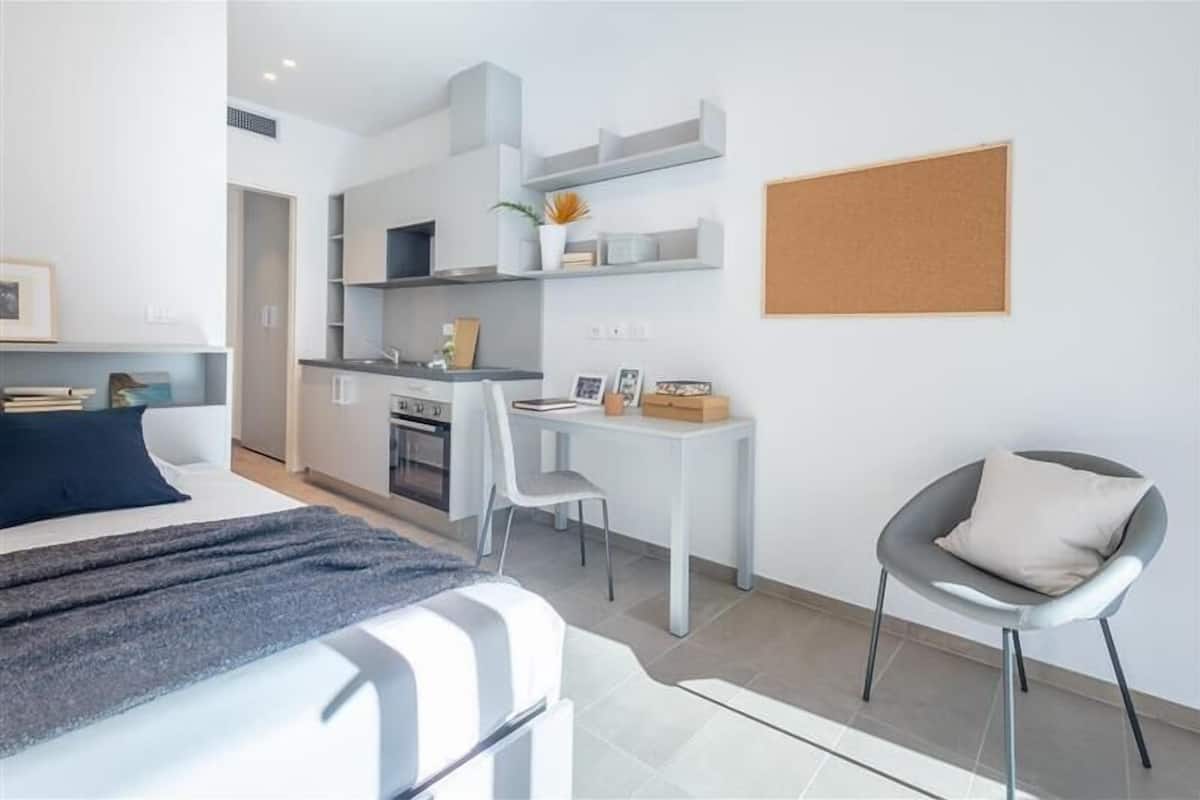 A modern, compact living space with a bed, a small kitchenette, a dining area, and a seating area.