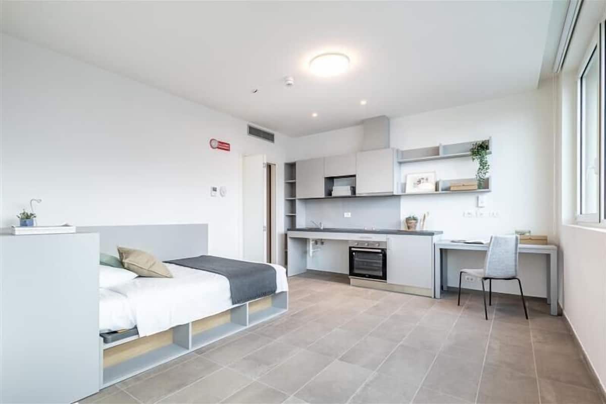 A compact studio apartment with a bed, kitchenette, and a desk area.