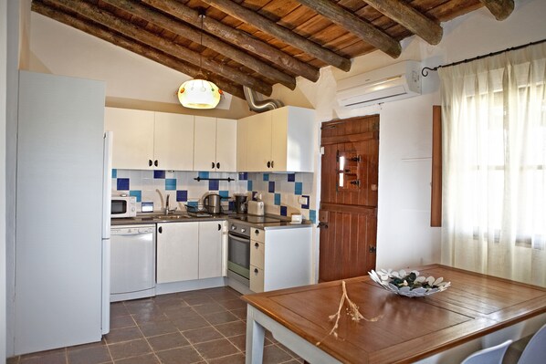 A kitchen with white cabinets, a wooden ceiling, a tiled backsplash, and a dining table with a bowl of fruit. - Herdade dos Mestres (Alandroal)