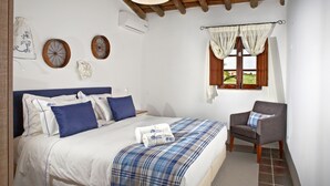 A bedroom with a bed, a chair, a window with curtains, and wall decorations. - Herdade dos Mestres (Alandroal)