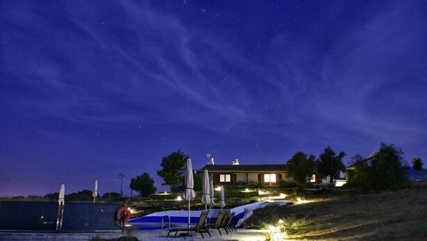 A nighttime view of a house with a swimming pool, lounge chairs, and a well-lit patio area. - Herdade dos Mestres (Alandroal)