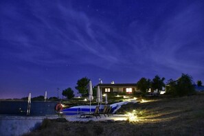 Ein Nachtbild eines Hauses mit Schwimmbad, Liegestühlen und einem gut beleuchteten Patio.