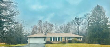 A single-story house with a garage, surrounded by a grassy yard and trees.