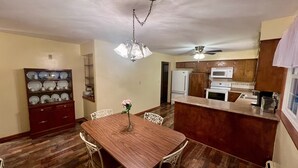 Zona pranzo con tavolo e sedie in legno, un lampadario e una cucina con elettrodomestici moderni.