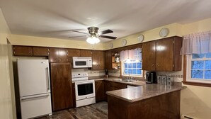 Una cucina con mobili in legno, frigorifero, forno a microonde, forno, lavello e finestra con tende.