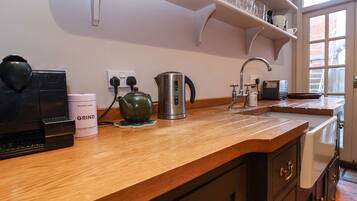 A kitchen with a wooden countertop, a kettle, a coffee maker, and a shelf with glassware.