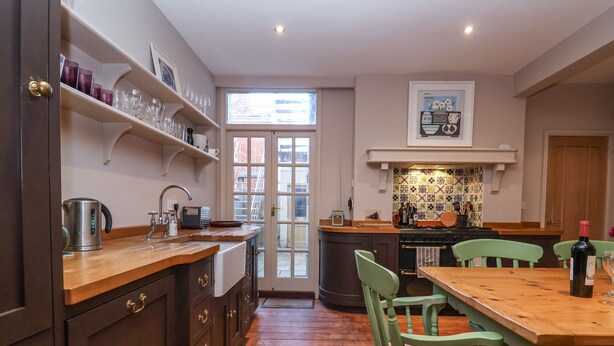 A kitchen with wooden cabinets, a sink, and a dining area with a table and chairs. - 11a Market Cross Place (Aldeburgh)