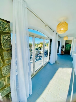 Enter a serene corridor leading to a balcony with a seating area and breathtaking views.