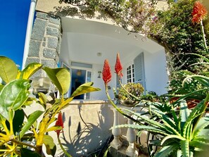 Guests can enjoy a serene outdoor setting with lush greenery and vibrant flowers surrounding the building's Mediterranean-inspired architecture.