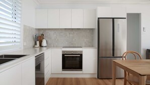 A modern kitchen with white cabinetry, a built-in oven, a stainless steel refrigerator, and a dining area with a wooden table and chairs.