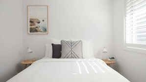 A minimalist bedroom with a bed, two bedside tables, a nightstand, a framed picture on the wall, and a window with blinds.