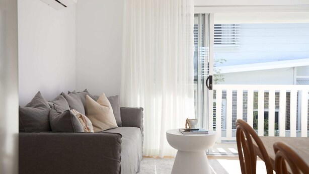 A modern living room with a grey sofa, a small white side table, and a view of a balcony with a white railing.