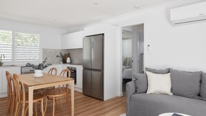 A modern kitchen with white cabinetry, a stainless steel refrigerator, and a dining area with wooden chairs and a table.