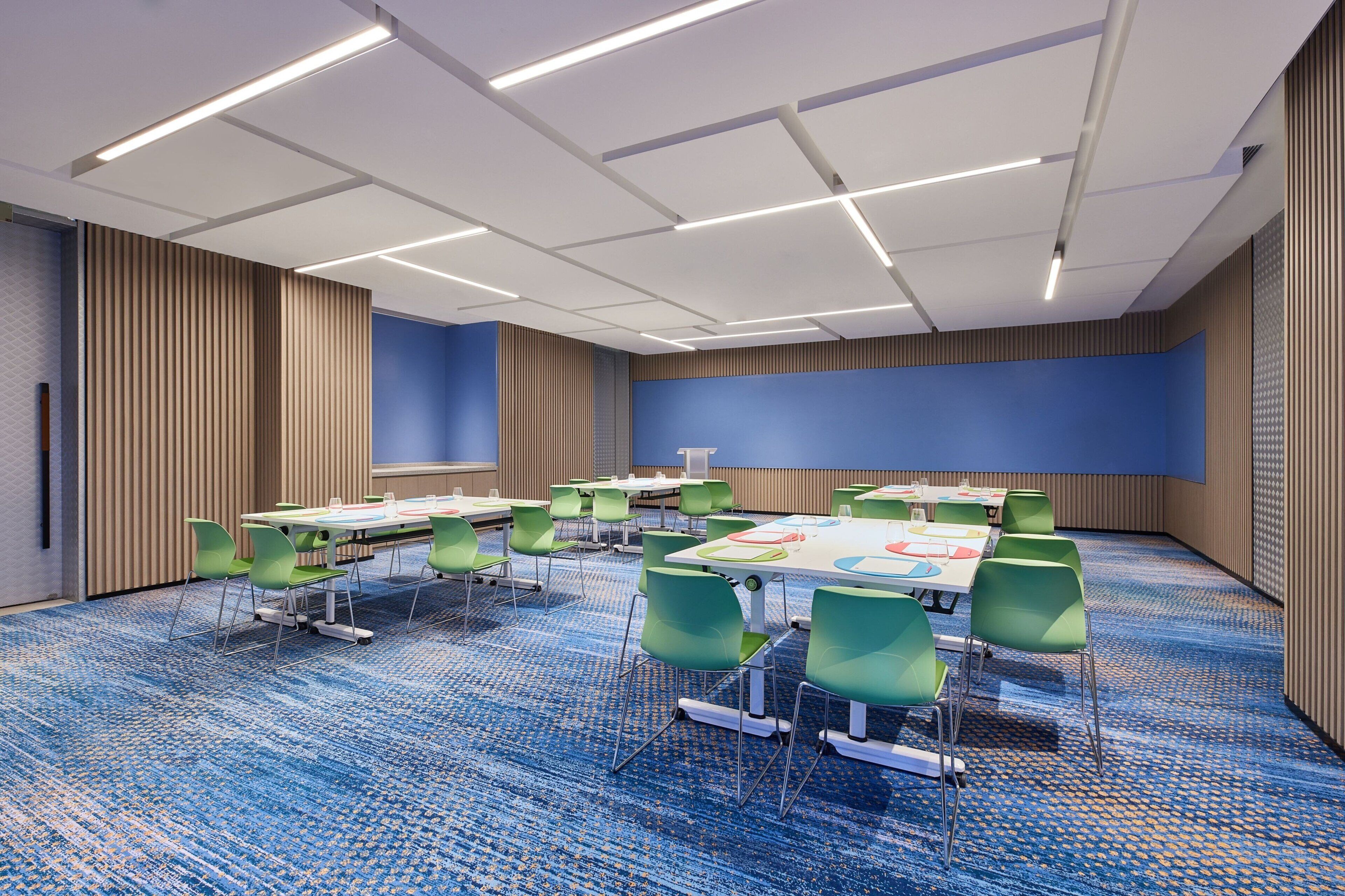 Un salón de conferencias con mesas, sillas y una pantalla grande.