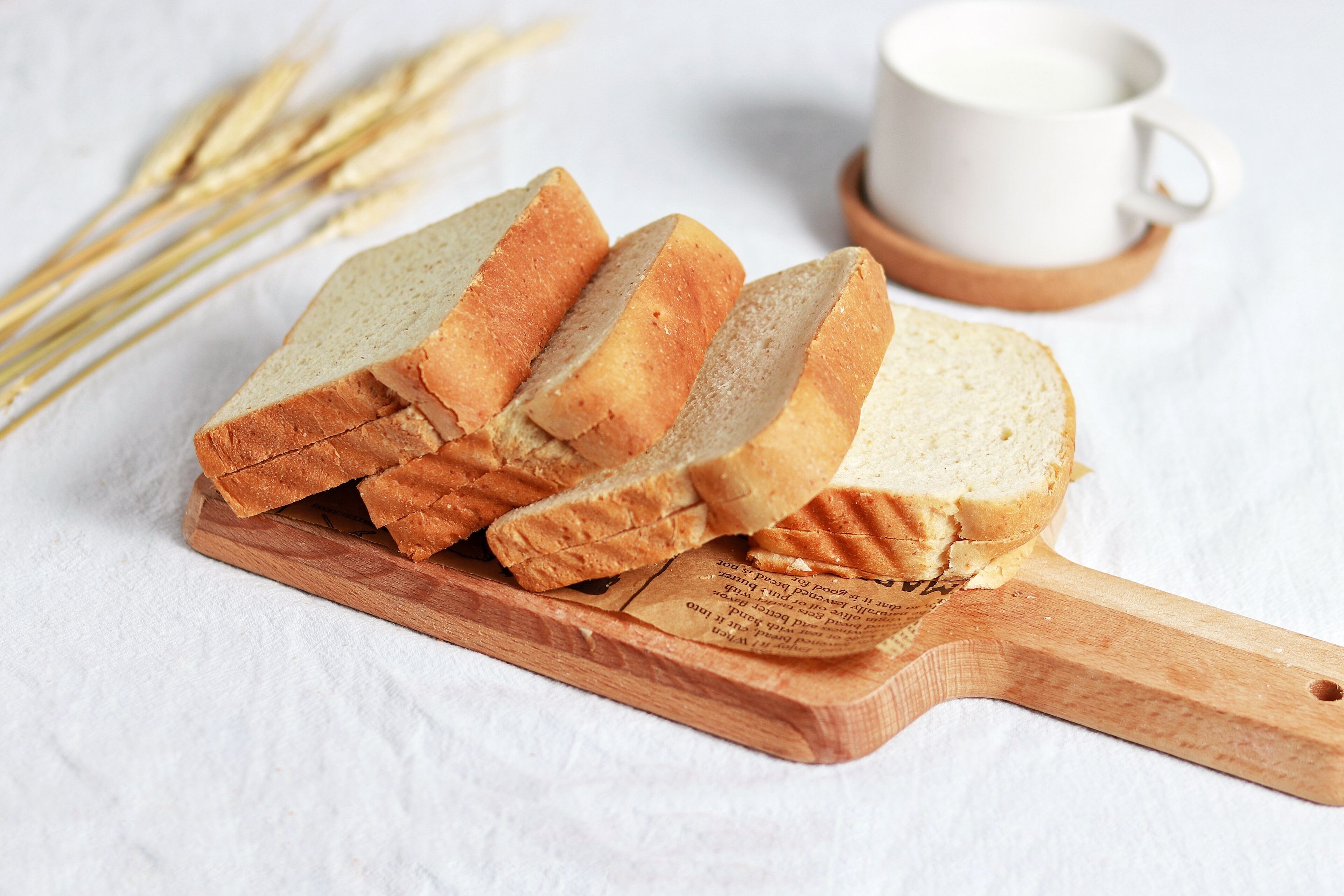 Slices of bread on a wooden cutting board with wheat stalks in the background.