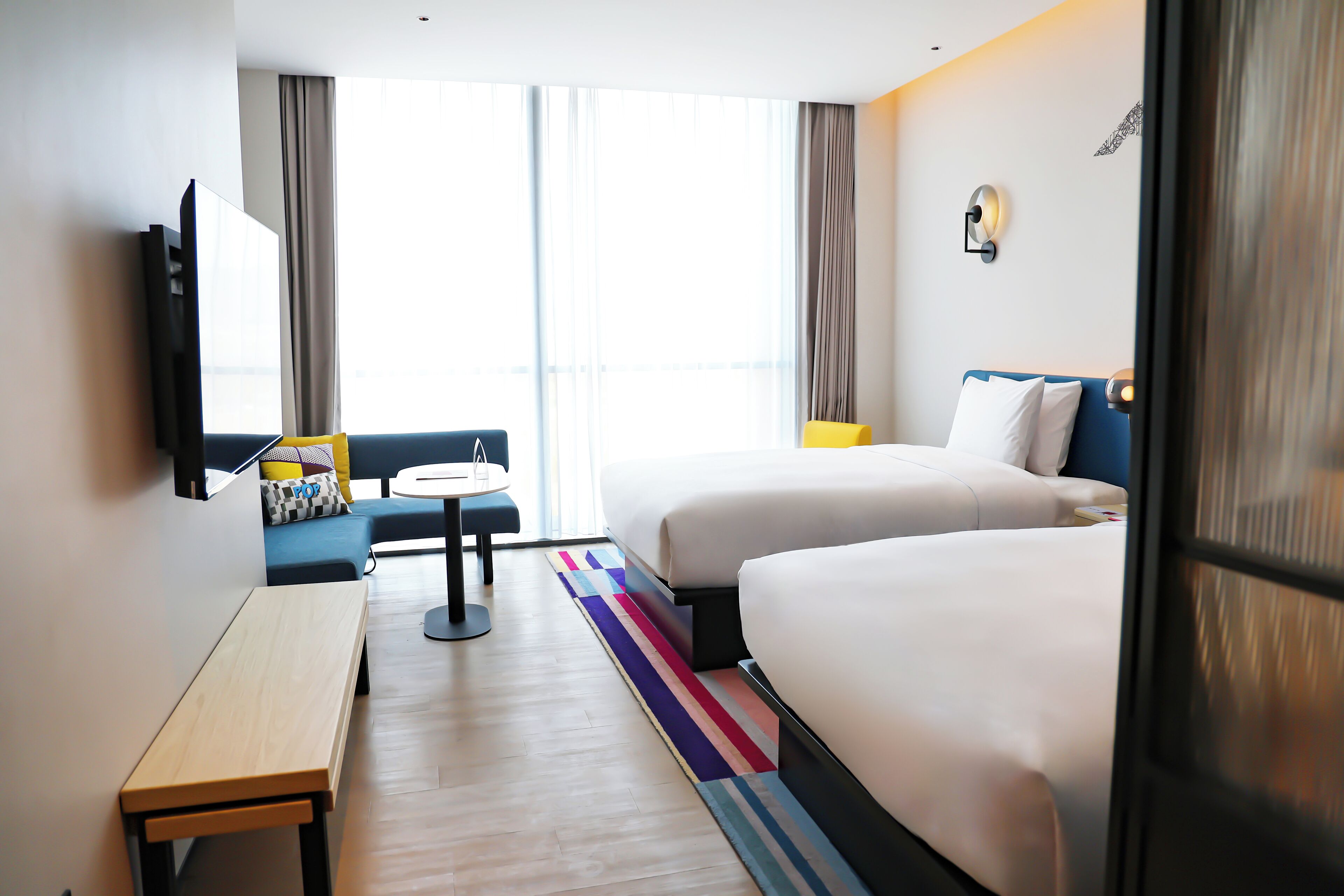 A hotel room with a bed, a desk, a chair, a small table, and a window with curtains.