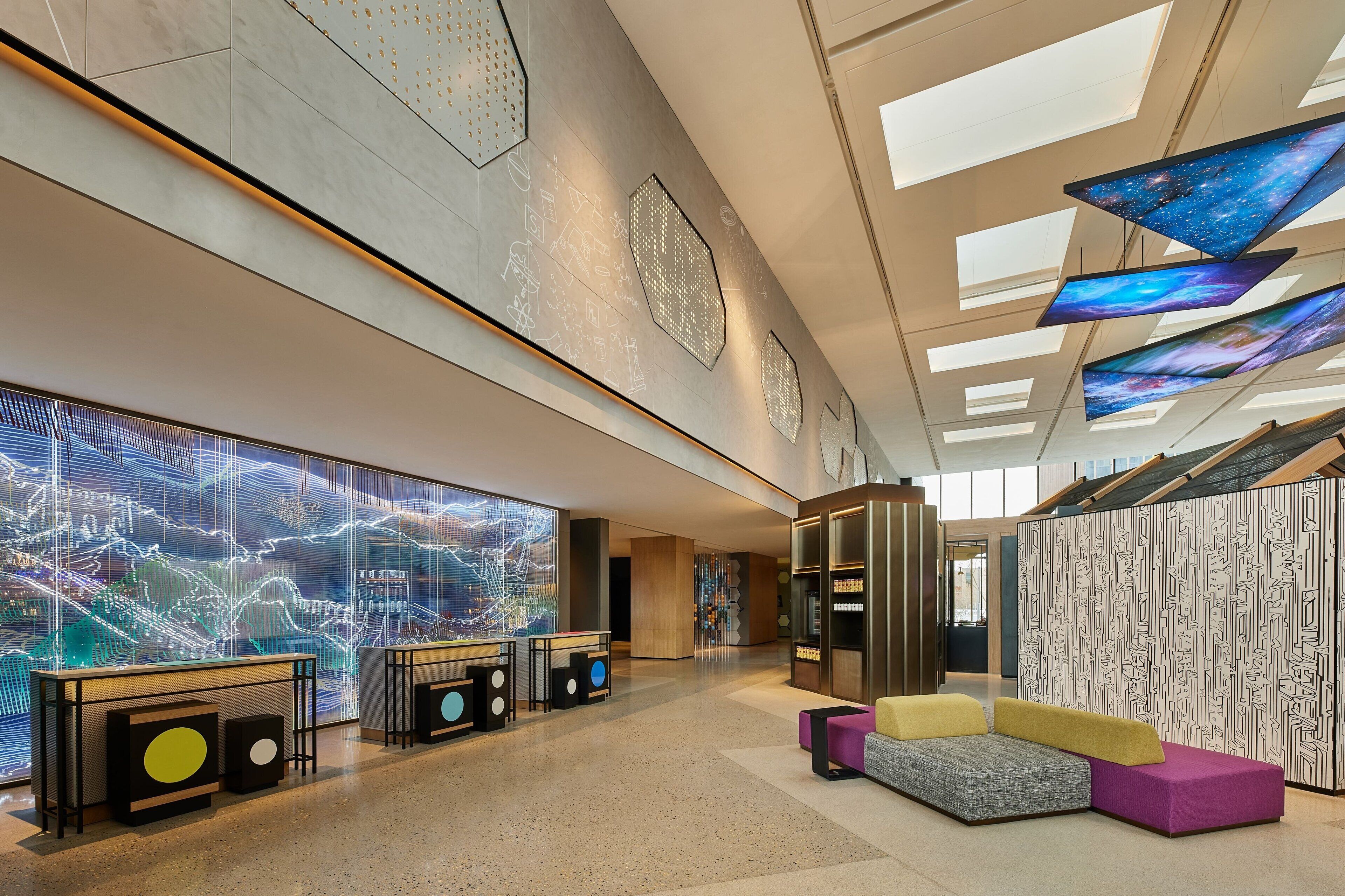 En rymlig entréhall med en stor digital skärm, sittgrupper och en modern arkitektonisk design.