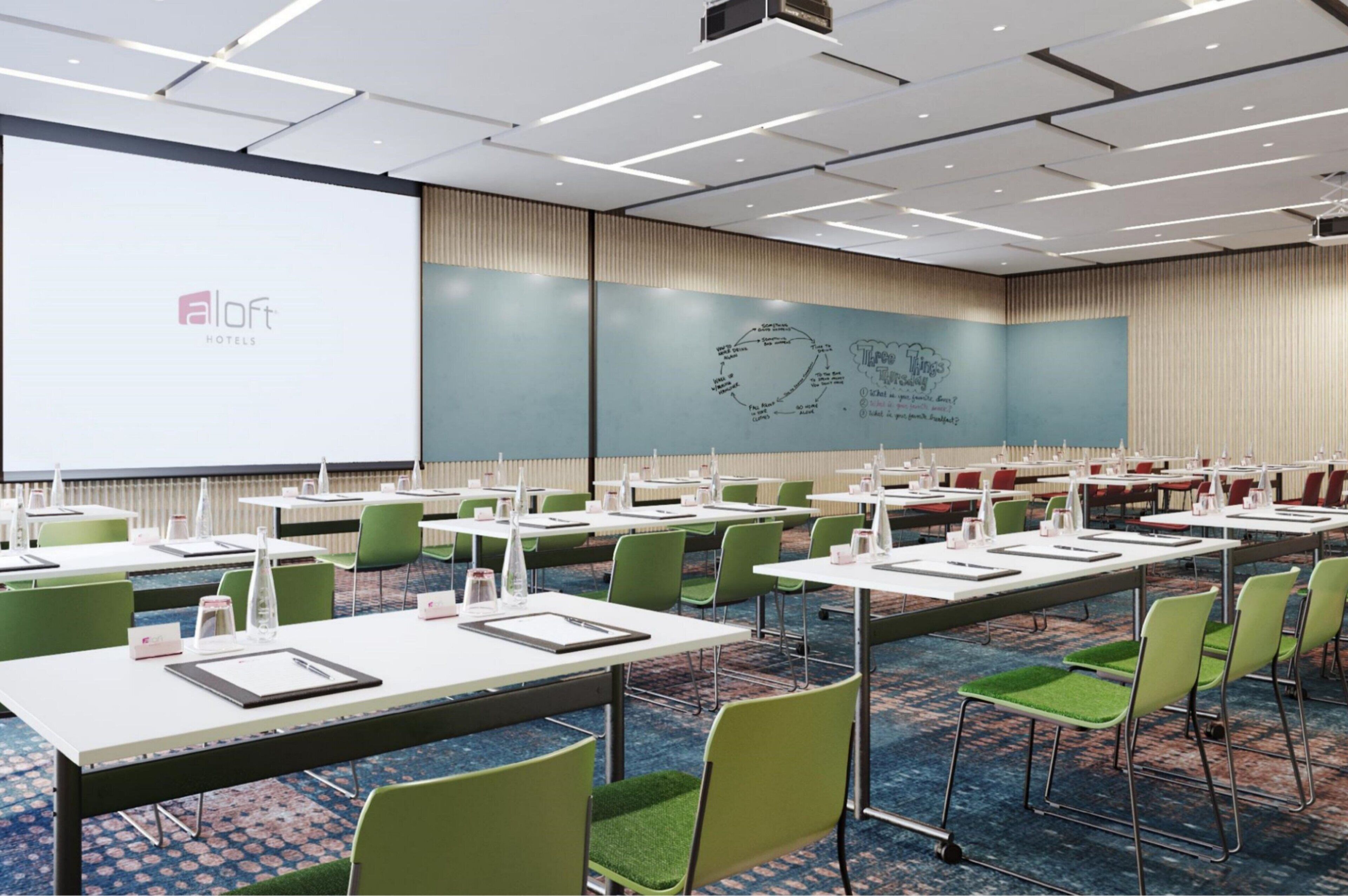 A conference room with multiple tables and chairs, a large screen, and a presentation on the wall.