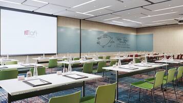 A conference room with multiple tables and chairs, a large screen, and a presentation on the wall.