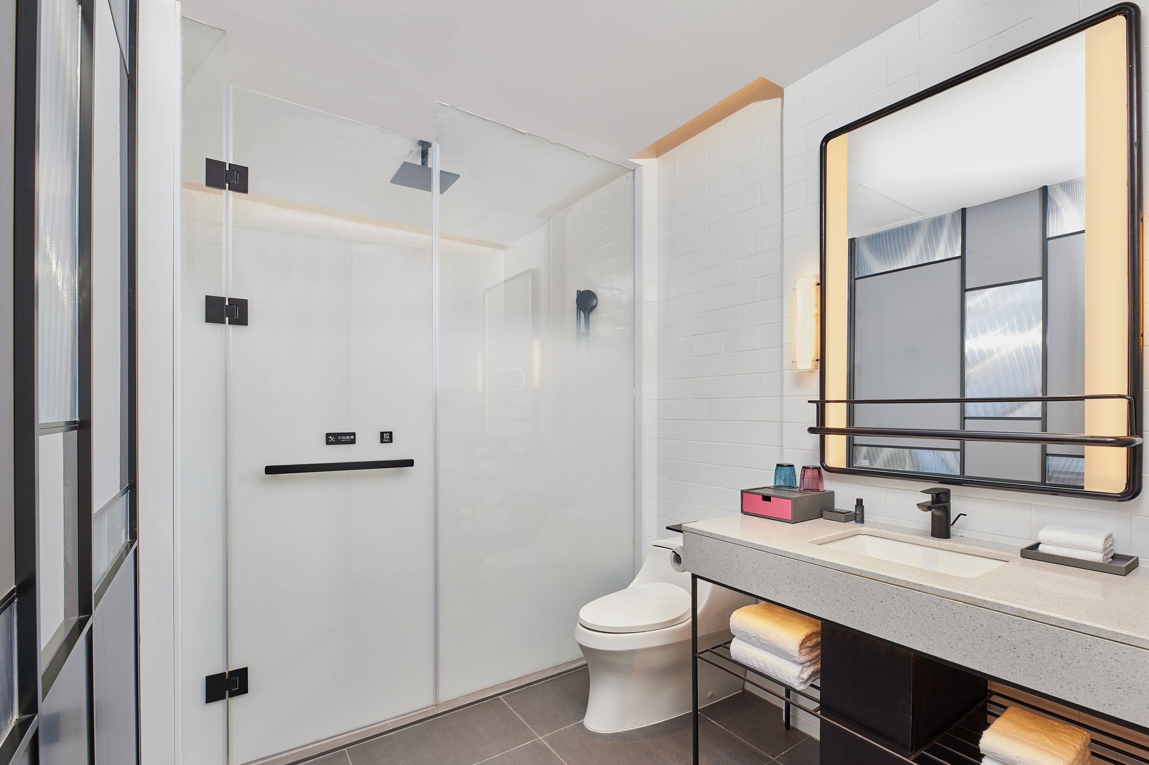 Een moderne badkamer met een douchecabine van glas, een wit toilet, een wastafel met spiegel en een handdoekrek.