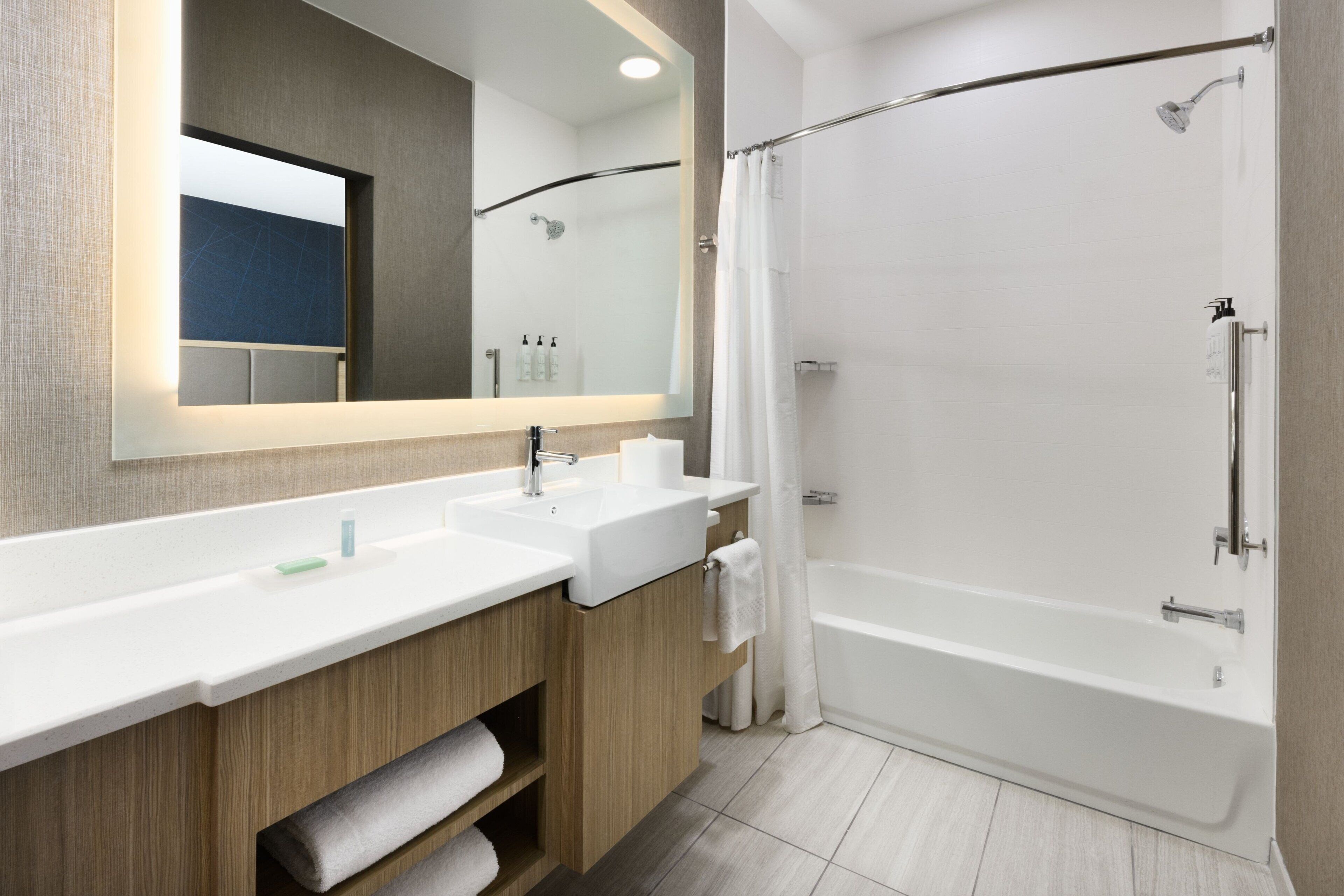 A modern bathroom with a large mirror, two sinks, a shower, and wooden cabinets.