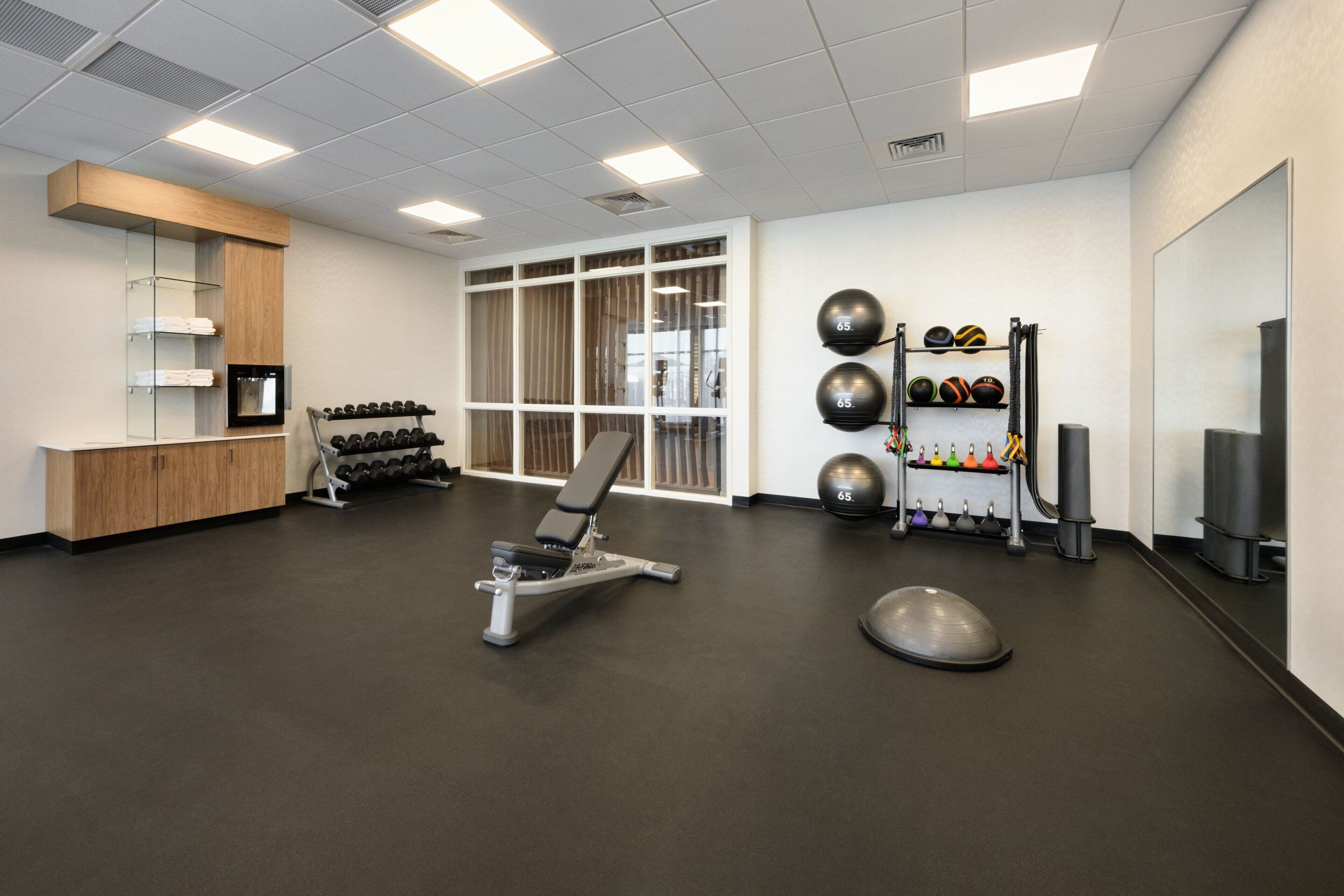 A gym with exercise equipment, a mirror, and a wall-mounted rack of dumbbells.