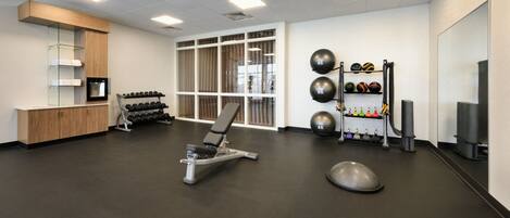 A gym with exercise equipment, a mirror, and a wall-mounted rack of dumbbells.