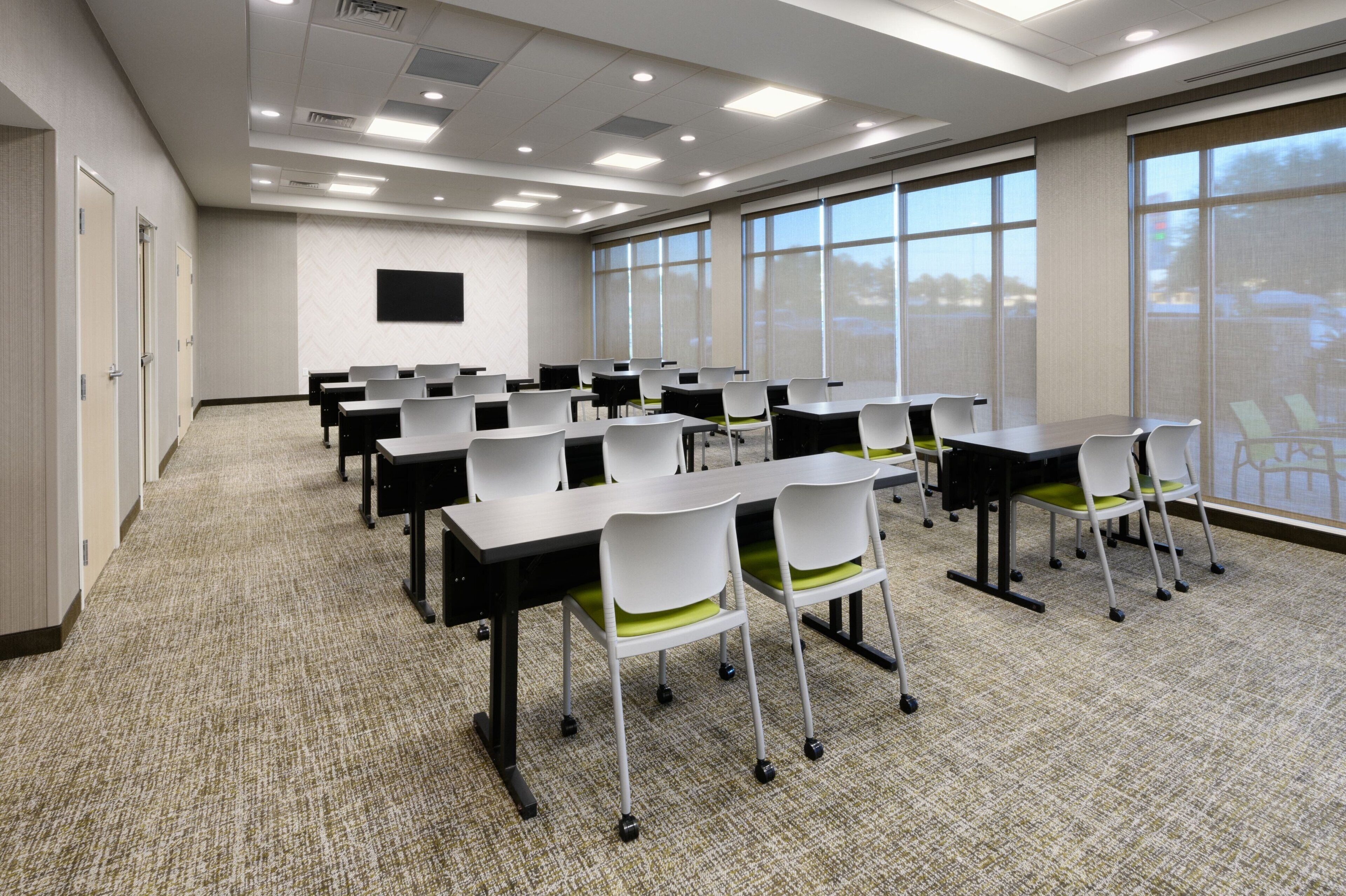 A conference room with tables and chairs, large windows, and a flat-screen TV on the wall.