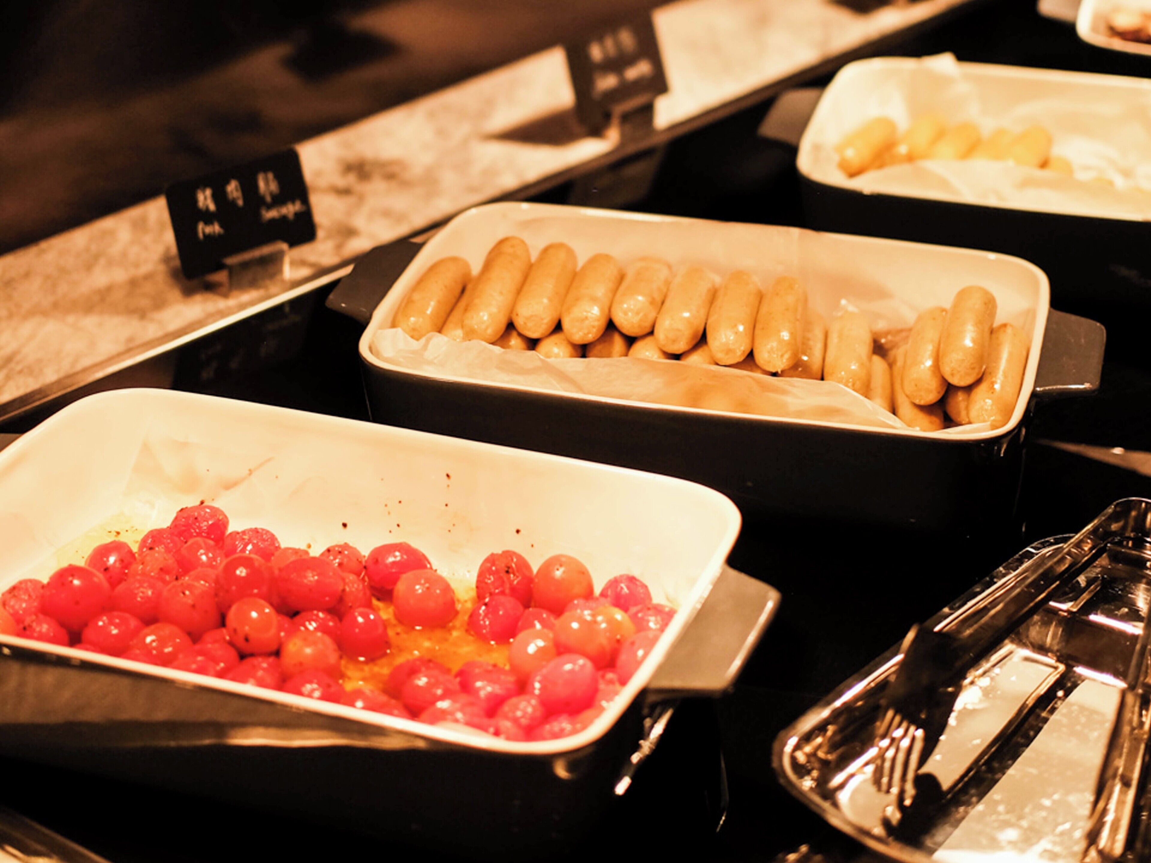 Un buffet proposant une variété de plats, notamment des saucisses, des tomates cerises et d’autres mets.