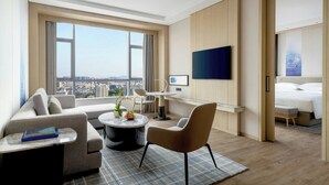 Une chambre d’hôtel moderne dotée d’une grande fenêtre, d’un téléviseur à écran plat, d’un canapé, d’une table à manger et d’un lit.