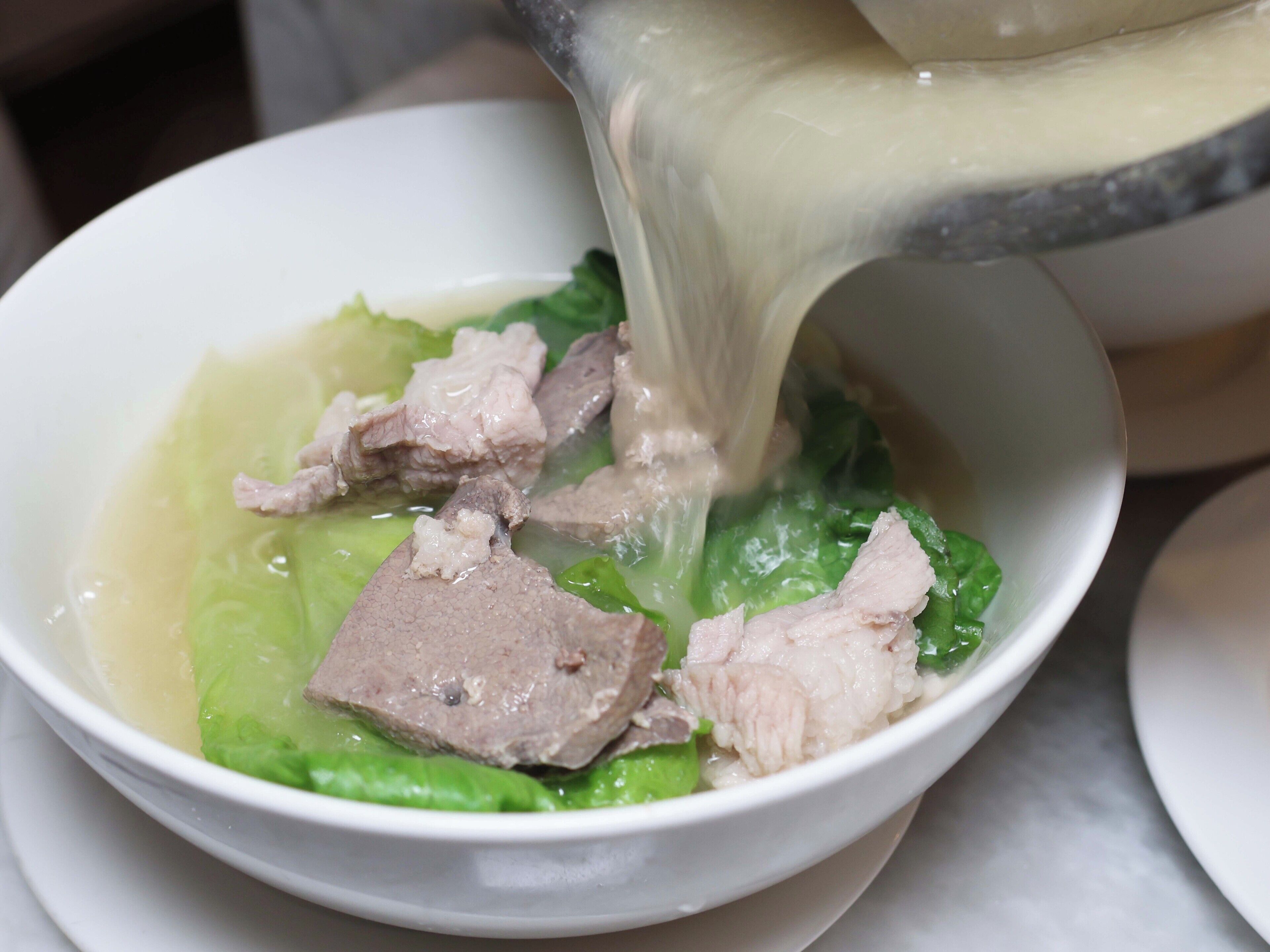 Eine Schüssel Suppe mit Fleisch und Gemüse, die aus einem Topf gegossen wird.