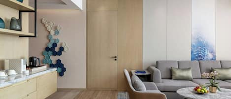 A modern living room with a grey sofa, a round coffee table with fruits, a small side table, and a decorative hexagonal wall piece.