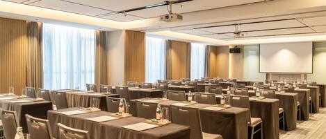 A conference room with multiple tables, chairs, a projector, and a screen.