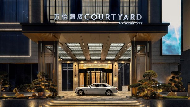 Une entrée d’hôtel moderne, avec une voiture garée devant, et une grande enseigne indiquant « COURTYARD BY MARRIOTT ».