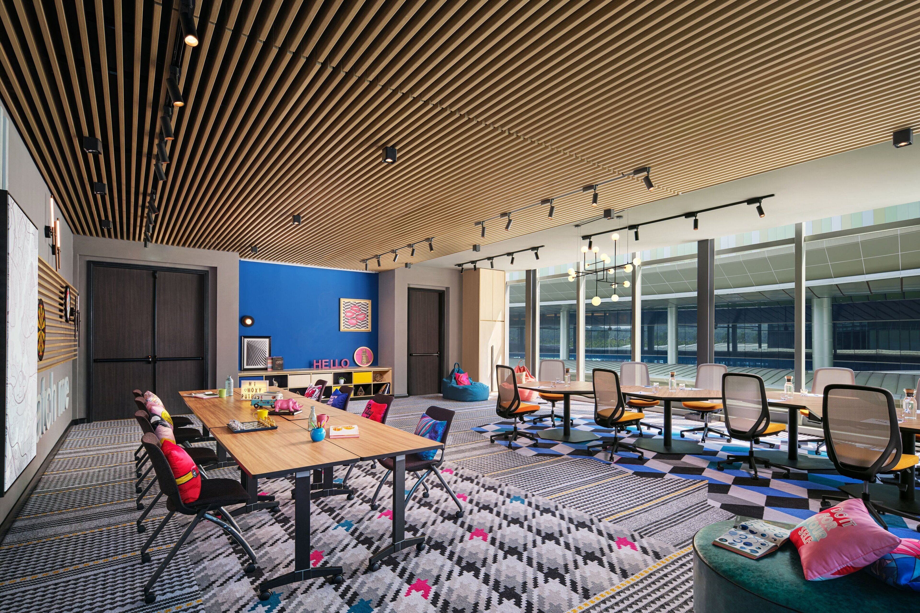 A modern meeting room with a wooden ceiling, large windows, and a colorful carpet.