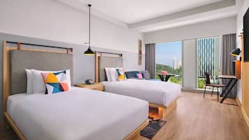 Quarto de hotel com duas camas, uma escrivaninha, uma cadeira e uma janela grande com vista para a cidade.