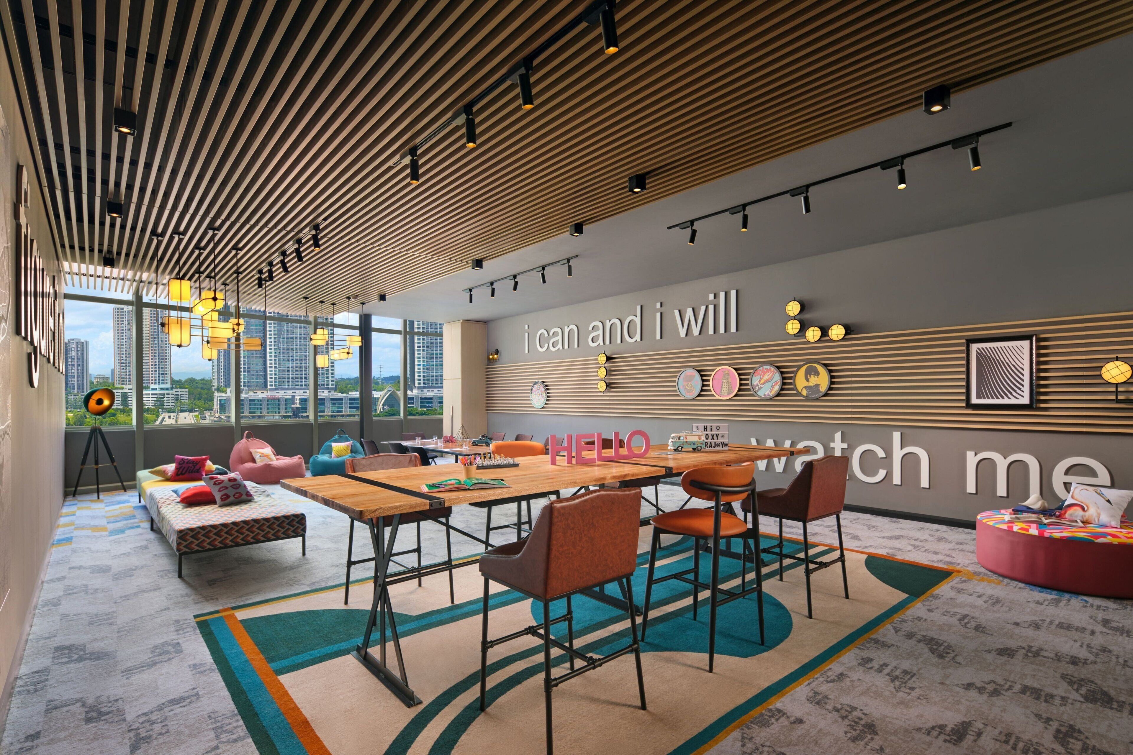 A modern office space with a wooden ceiling, a large window offering a city view, a wooden table with chairs, and a colorful carpet.
