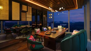 Un comedor moderno con una mesa de madera, sillas verdes y vistas a la ciudad a través de amplias ventanas.
