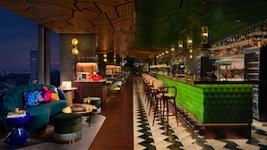 Zona de bar moderna con mostrador tapizado en verde, techo de madera y vistas a la ciudad.