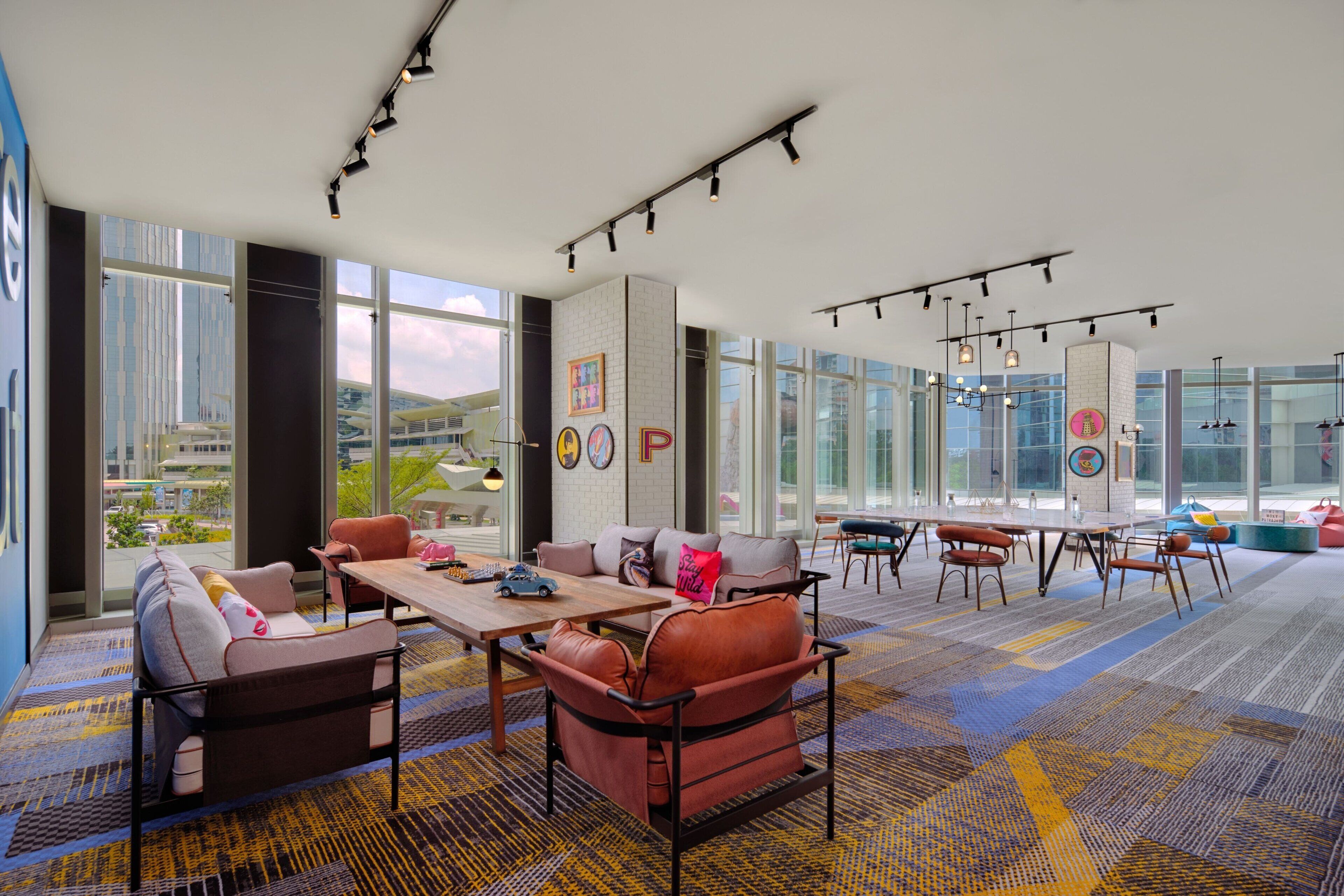 A spacious, modern lounge area with a large table, comfortable seating, and large windows offering a city view.