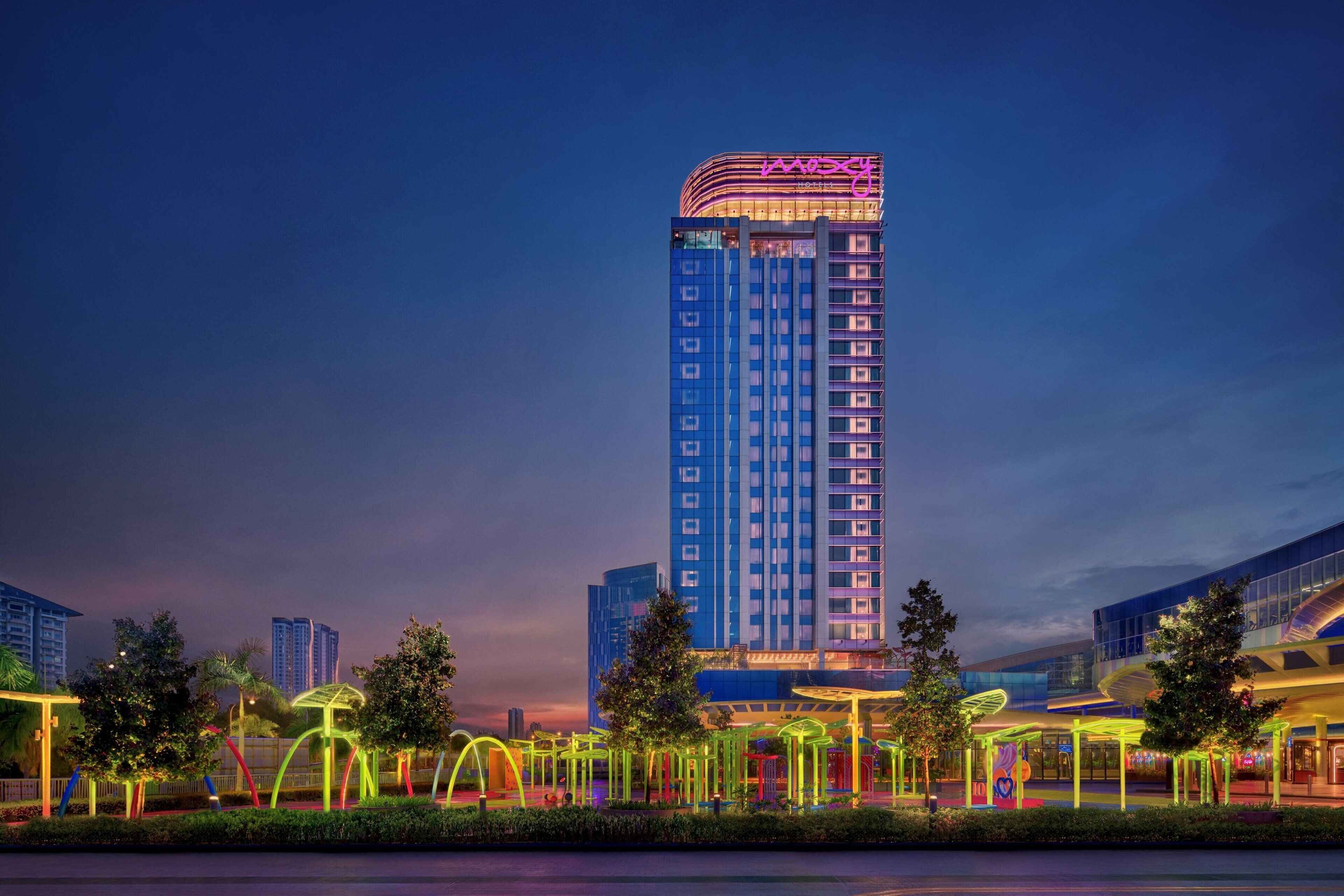 A high-rise hotel with a modern design, featuring a prominent neon sign on the top.