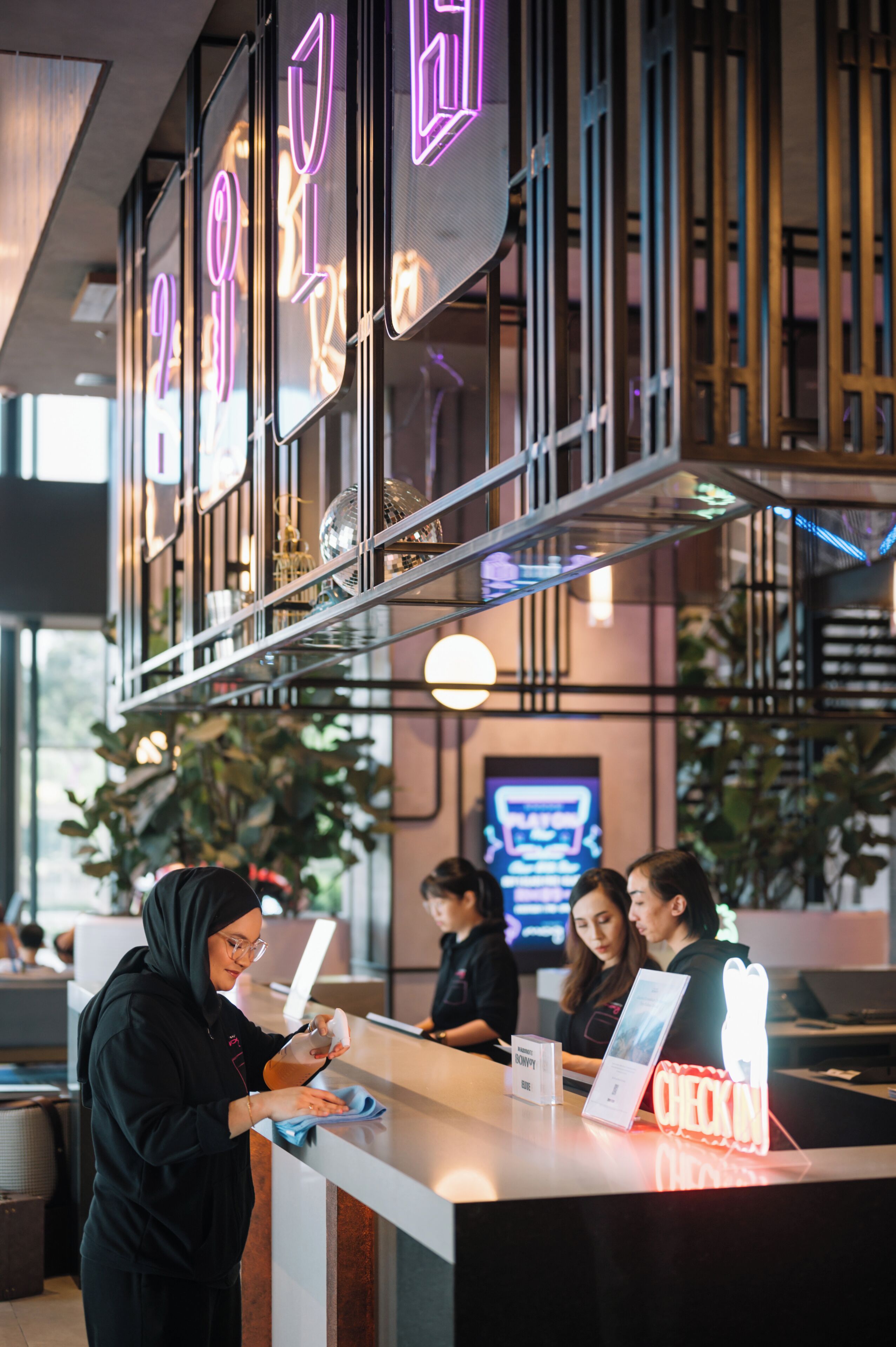 A reception area with a counter, a neon sign, and a staircase in the background.
