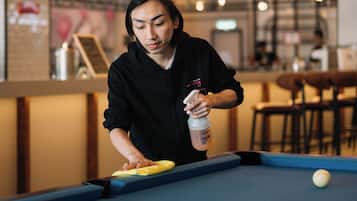 Une personne est en train de nettoyer une table de billard dans une pièce où l’on aperçoit, à l’arrière-plan, une enseigne au néon.
