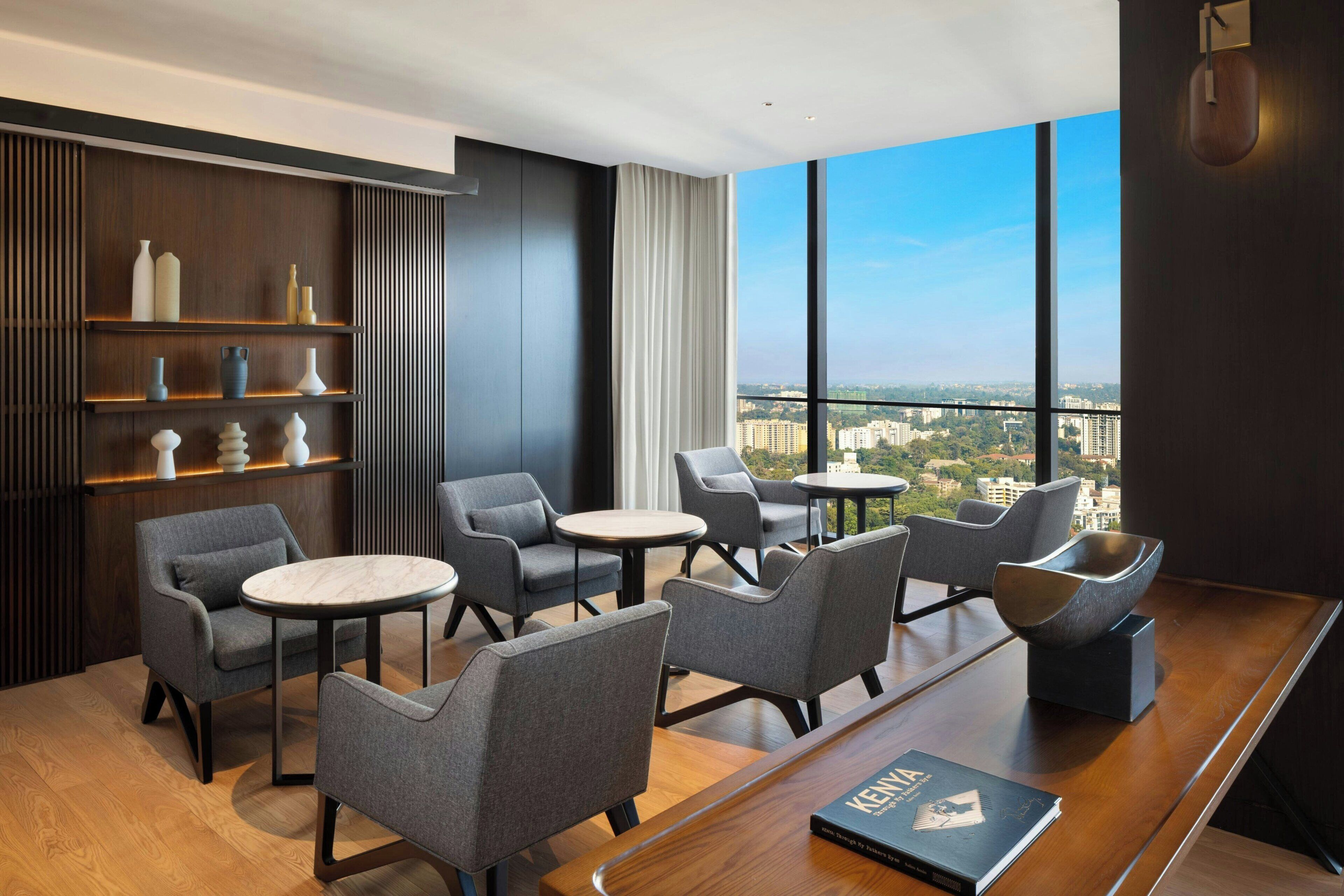 A modern lounge with grey upholstered chairs, a wooden coffee table, and a bookshelf with decorative items.