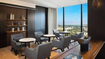 A modern lounge with grey upholstered chairs, a wooden coffee table, and a bookshelf with decorative items.